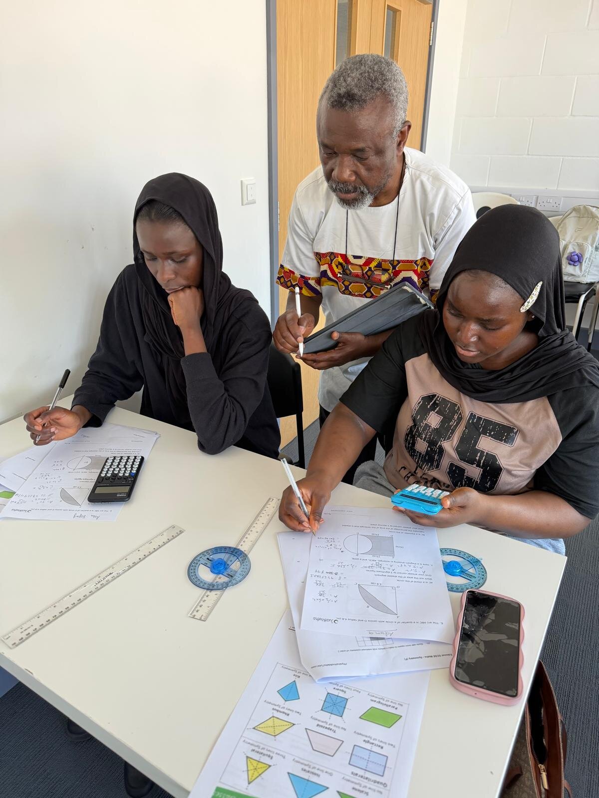 Sylvester Peprah guiding two students through GCSE geometry worksheets in the classroom